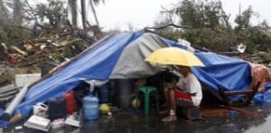A typhoon victim sits under an umbrella outside a makeshift tent after Super Typhoon Haiyan battered Tacloban city in central Philippines
